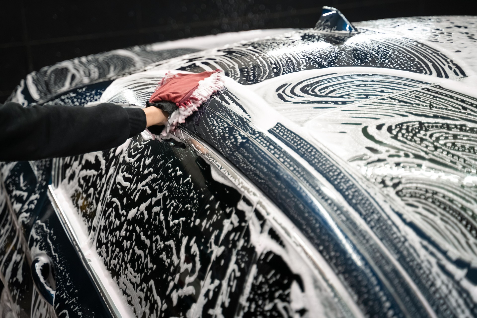 Professional car wash. Detailing worker washes the vehicle body with foam and rag